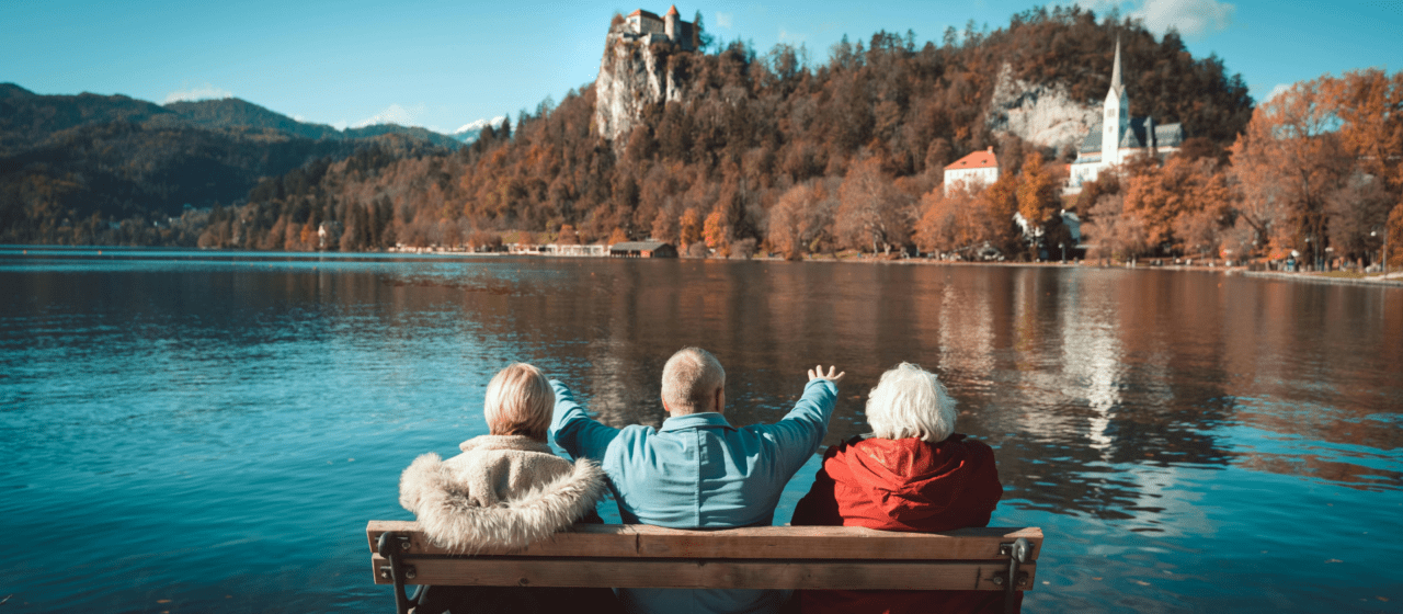 Three retirees relaxing on a bench overlooking a lake and autumn mountains, enjoying a secure retirement