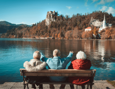 Three retirees relaxing on a bench overlooking a lake and autumn mountains, enjoying a secure retirement