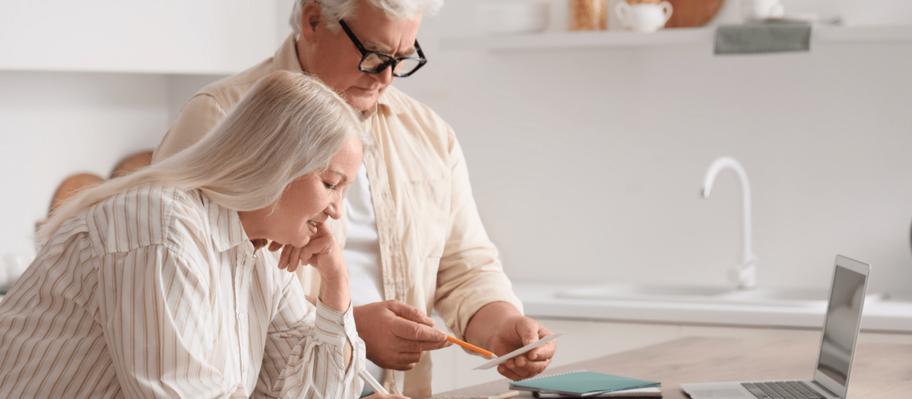 Retired couple reviewing paperwork, calculator, and laptop at their kitchen table while planning their RMD strategy