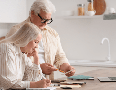 Retired couple reviewing paperwork, calculator, and laptop at their kitchen table while planning their RMD strategy